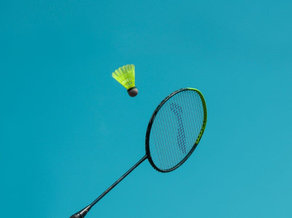 Black and neon-green badminton racket with a lime shuttlecock against a cyan blue background