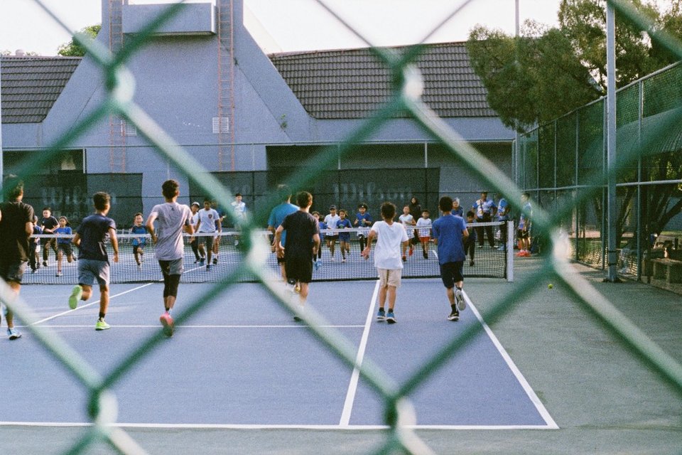 Junior tennis players running drills on an outdoor blue court